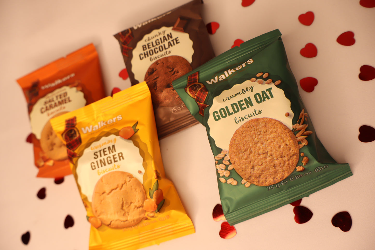 Four packets of Walkers biscuits on a light background with heart shapes.