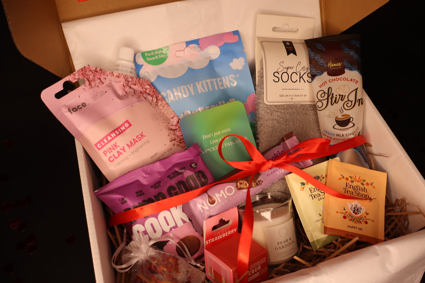 Assorted items including a clay mask, candy kittens, socks, and tea in a box with a red ribbon.
