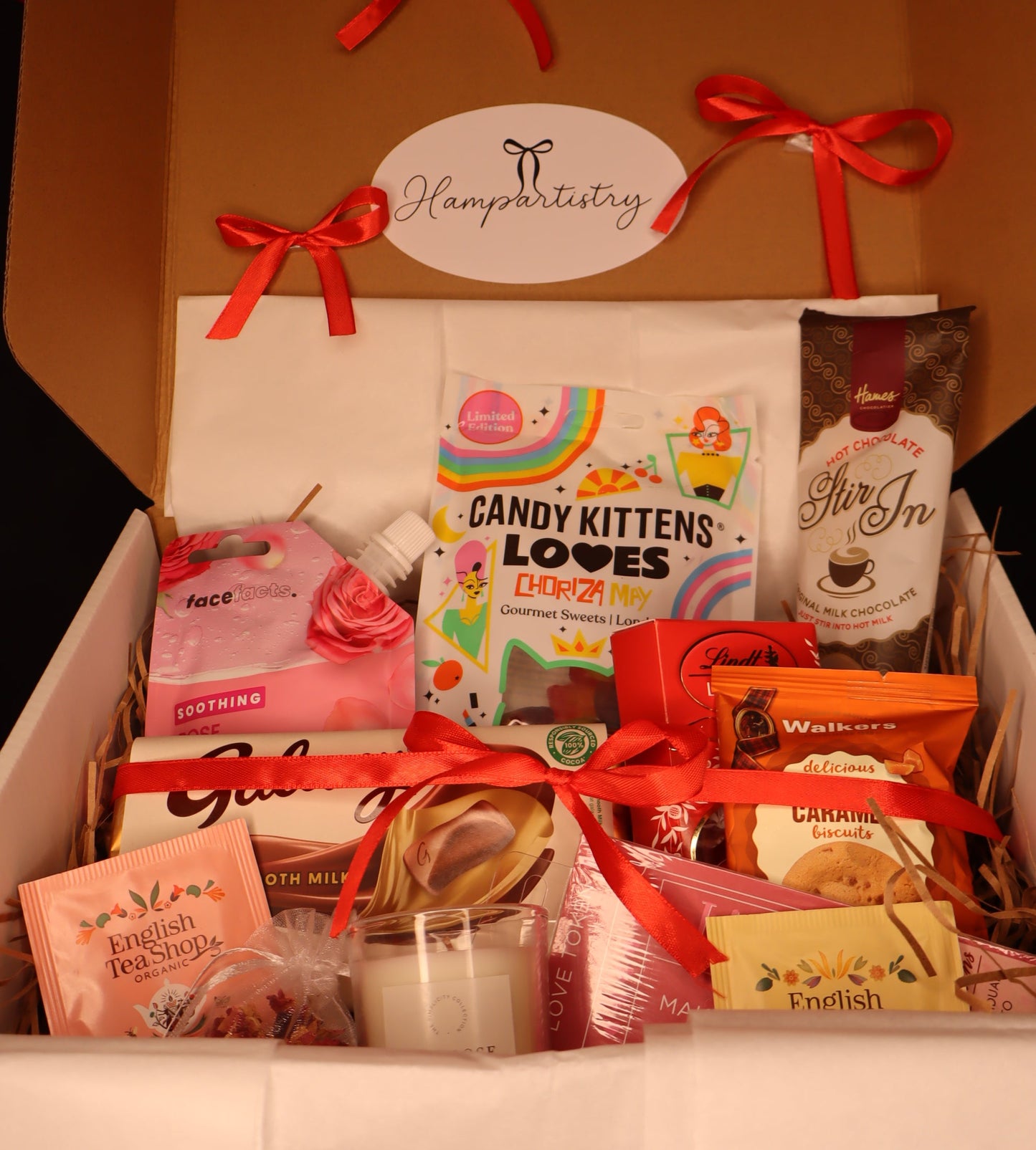 Gift box with various items including pamper essentials and chocolate treats, tied with red ribbons.