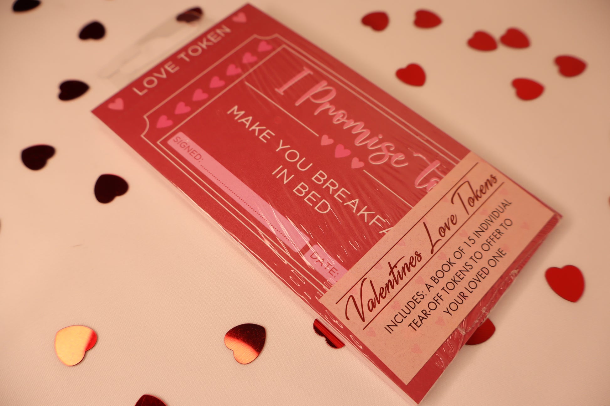 Valentine's Day-themed love token book with heart confetti on a light background