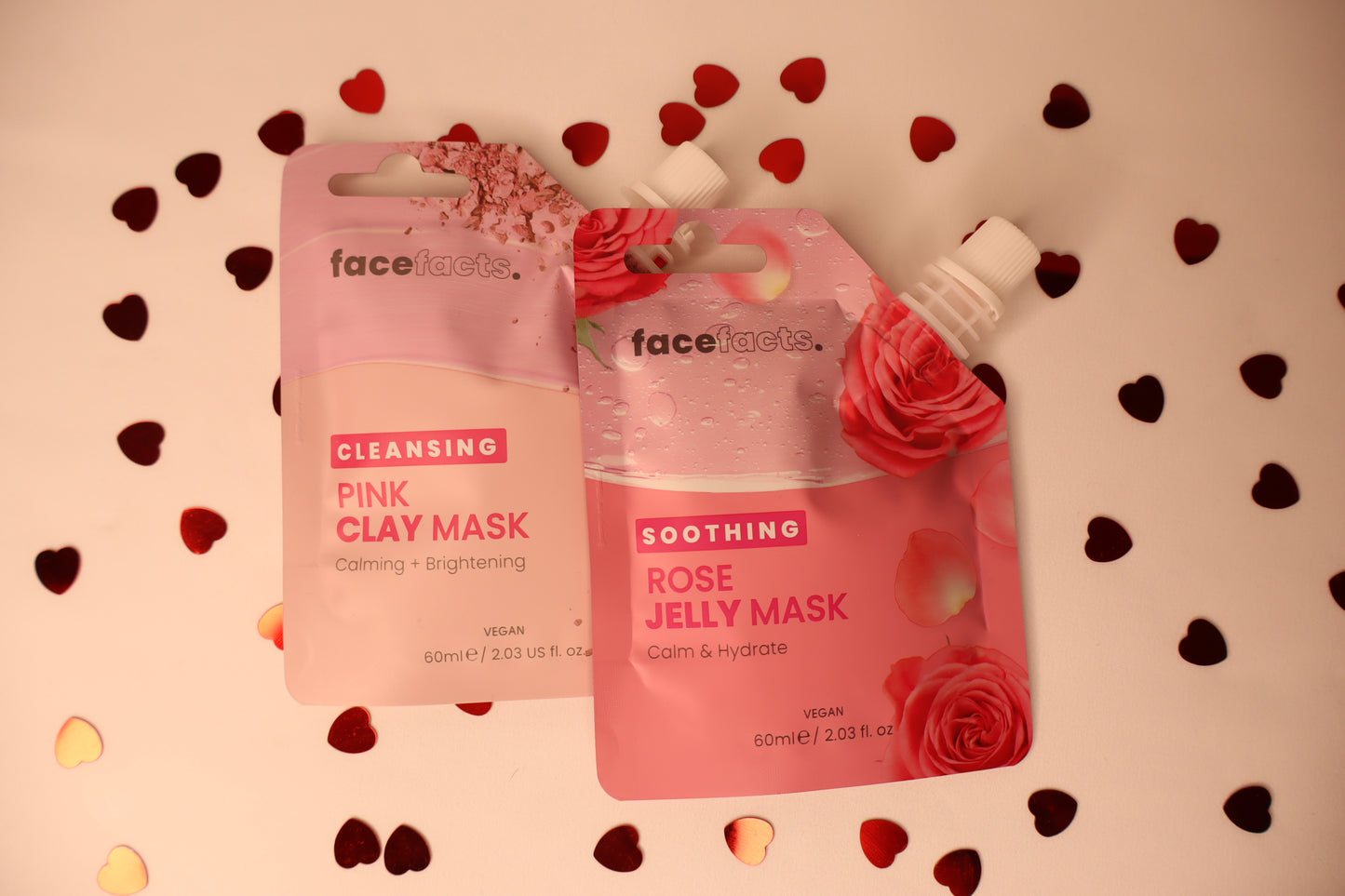 Two facial mask packages from Face facts on a decorative background with heart shapes.