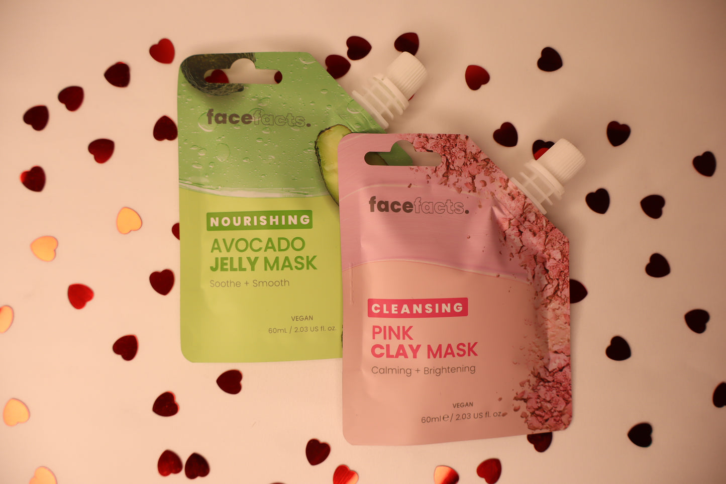 Two facial mask packages, one green and one pink, on a background with heart confetti
