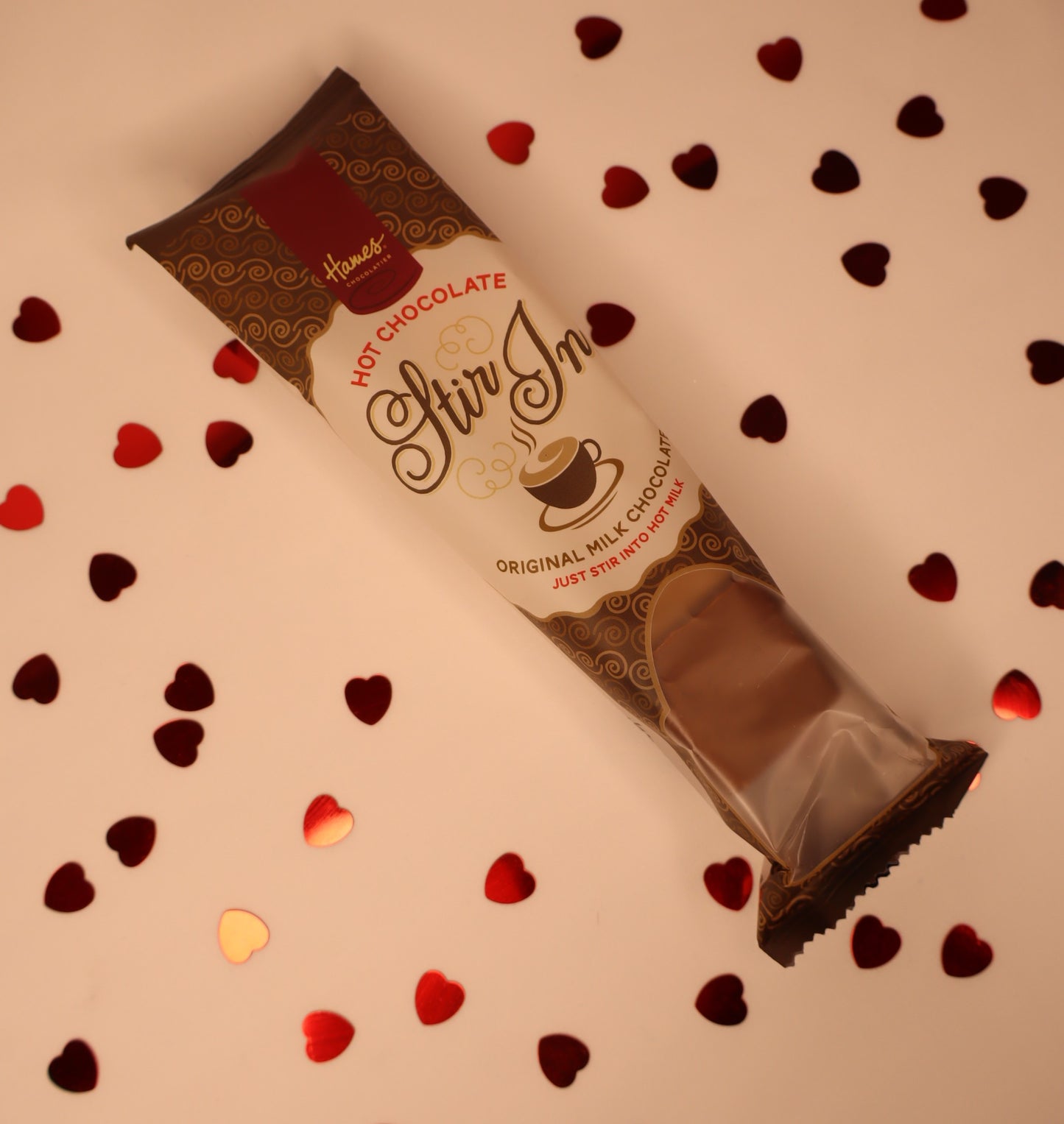 Hot chocolate stir-in package with heart-shaped confetti on a white background