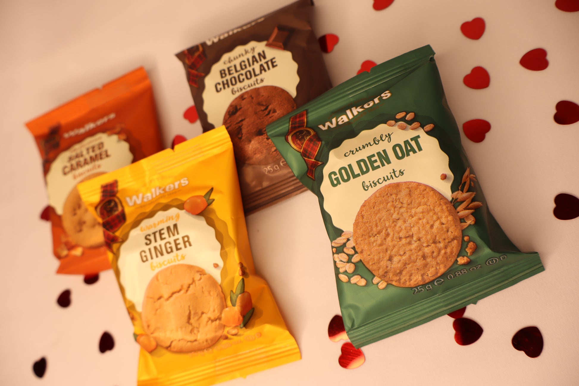 Four packets of Walkers biscuits on a light background with heart shapes.