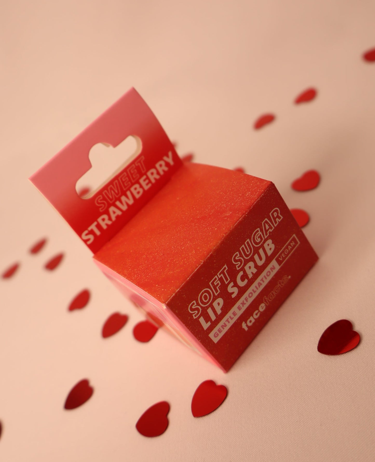 Red lip scrub packaging with 'Strawberry' text on a pink background with heart shapes.