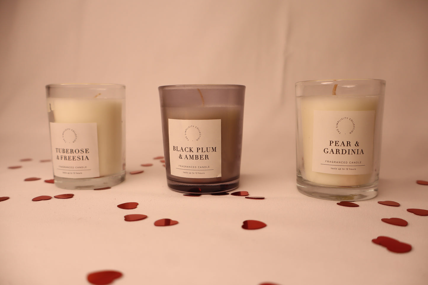 Three candles with labels on a surface with red hearts
