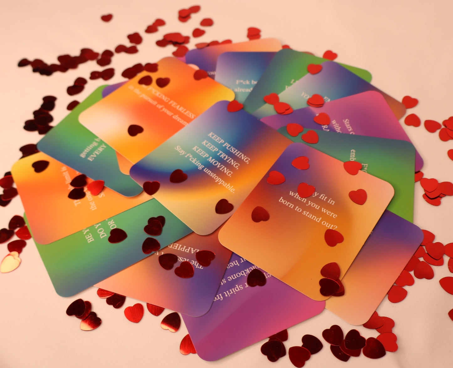 Colorful cards with motivational phrases on a pink background with red heart-shaped confetti.